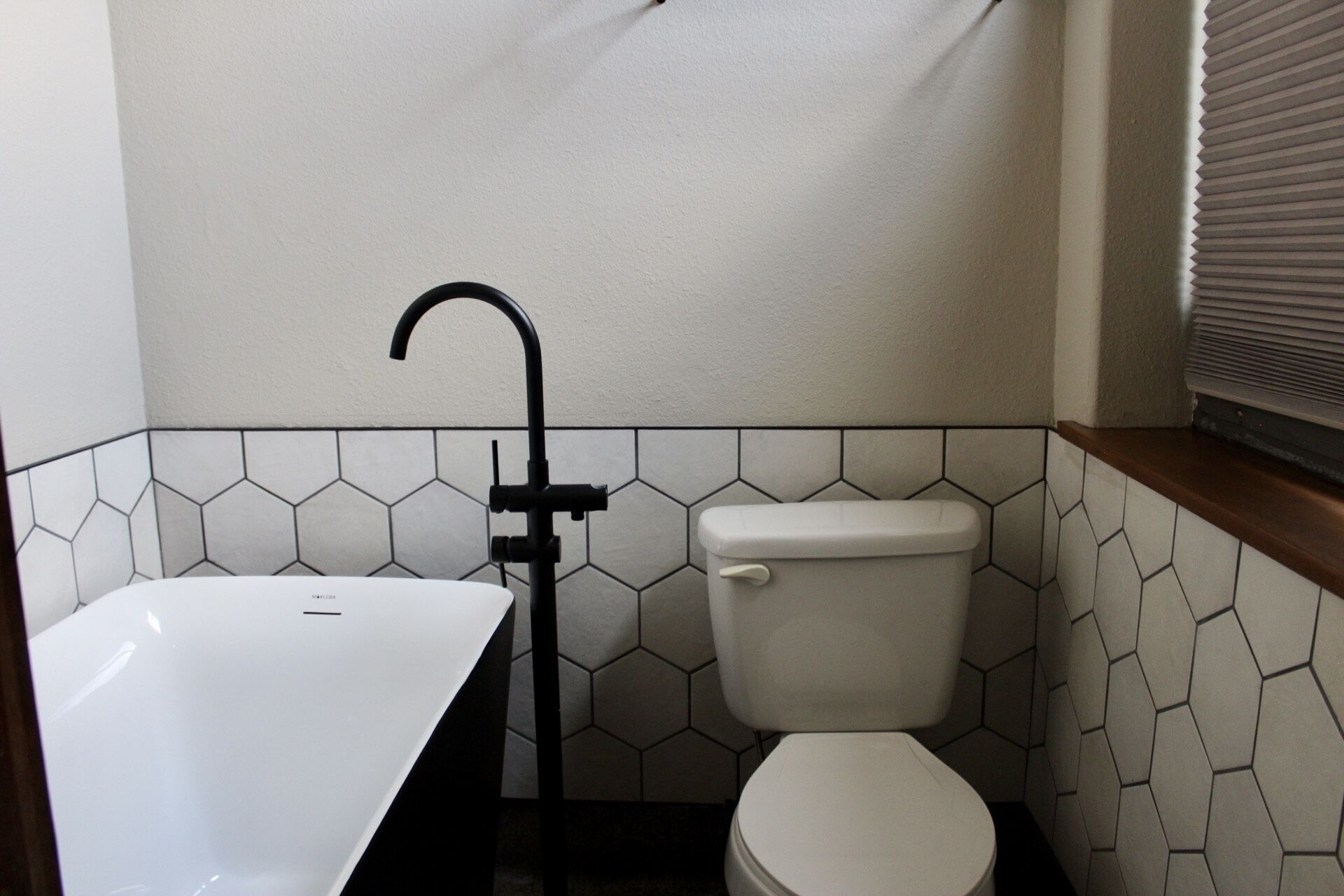 Ein Badezimmer mit Toilette, schwarzem Wasserhahn und Waschbecken. Die Wände sind mit sechseckigen Fliesen versehen.