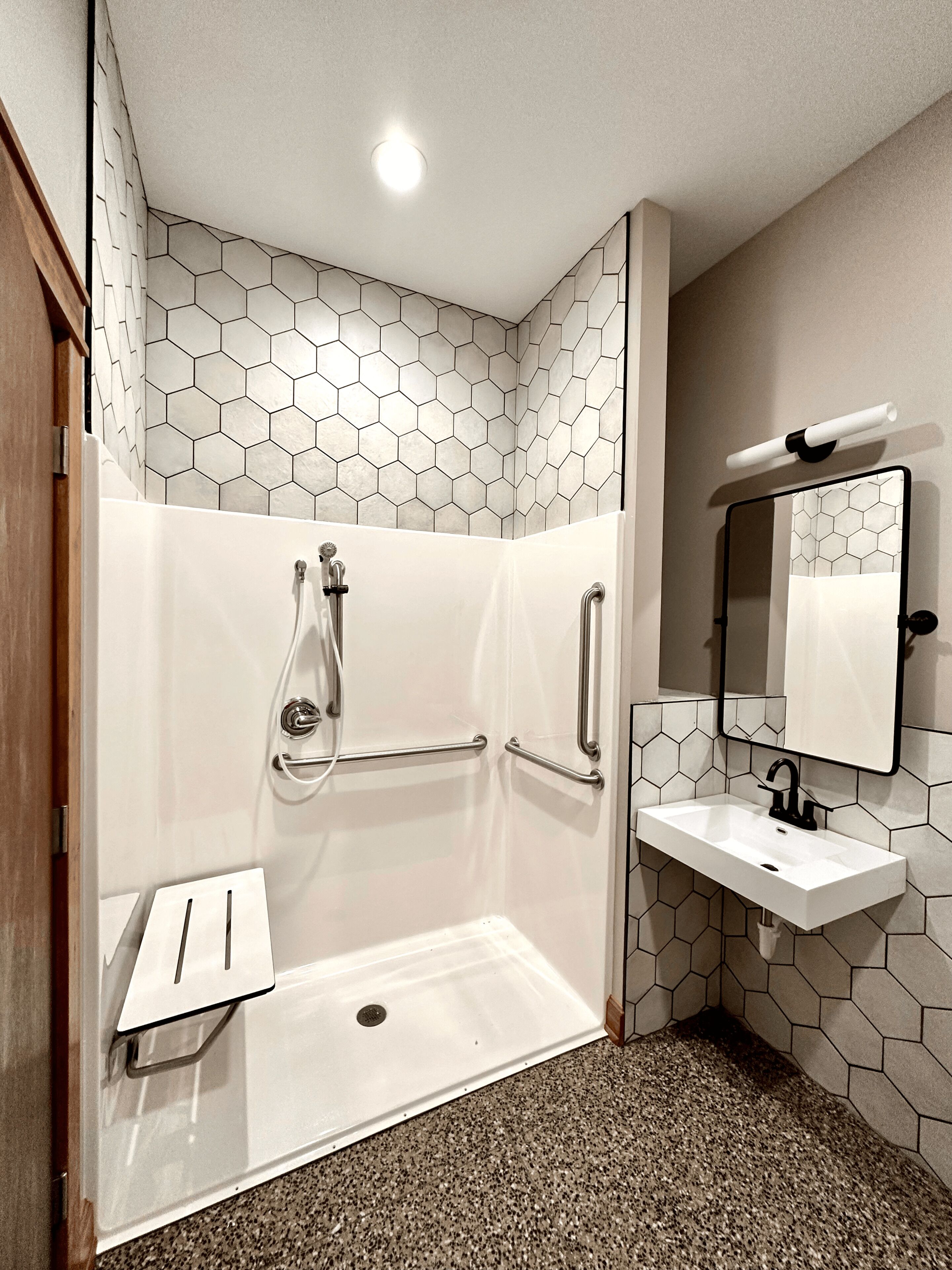 A modern bathroom with a shower, grab bars, a sink, and a mirror.