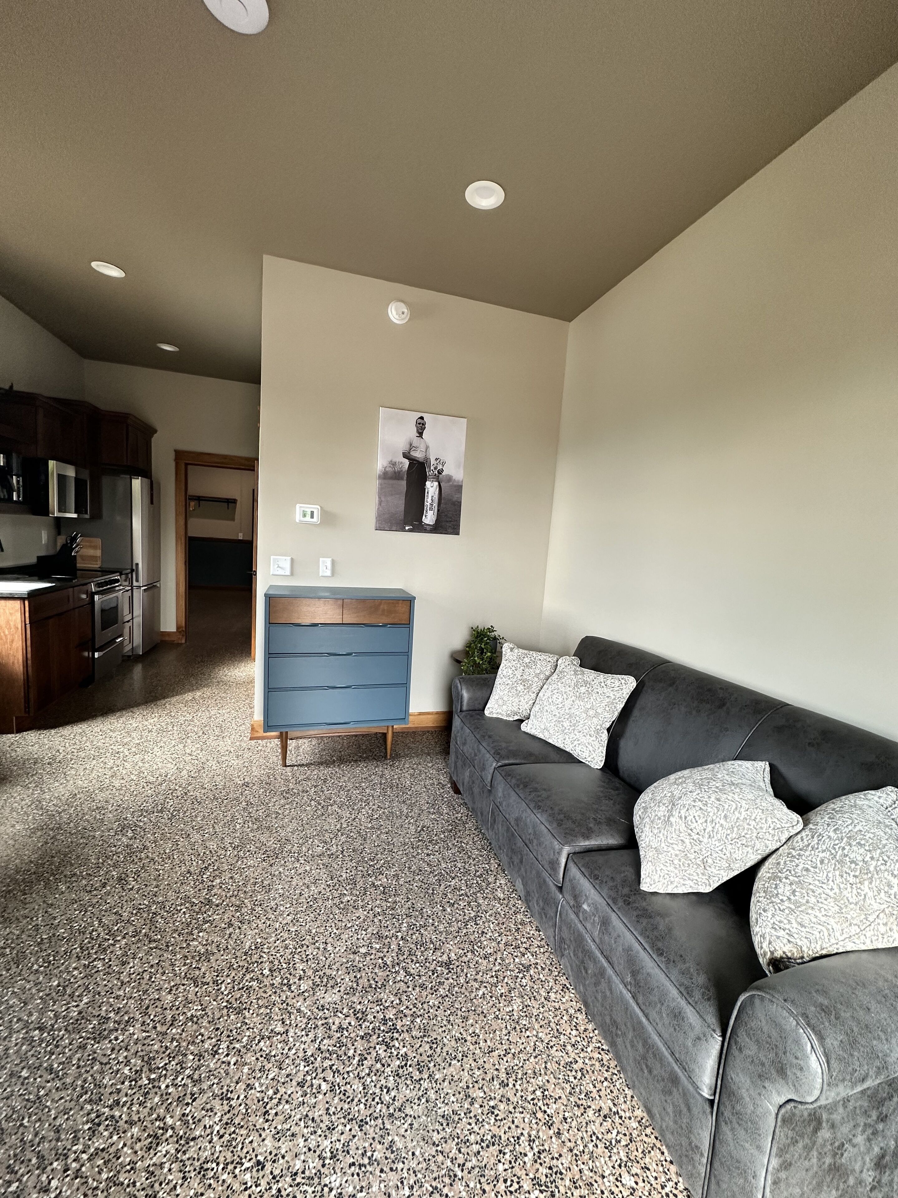 Un salon moderne avec un canapé gris foncé, une commode bleue et une cuisine en arrière-plan.