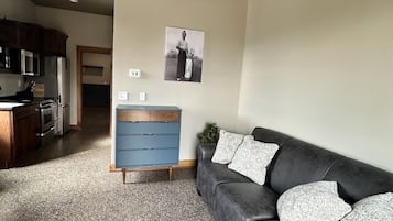 Un salon moderne avec un canapé gris foncé, une commode bleue et une cuisine en arrière-plan.
