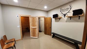 A room with a wooden bench, a bench with a black backrest, a wall-mounted shelf with towels, a door, and a wall decal of antlers with the text "The Lodge Luxury Suites".