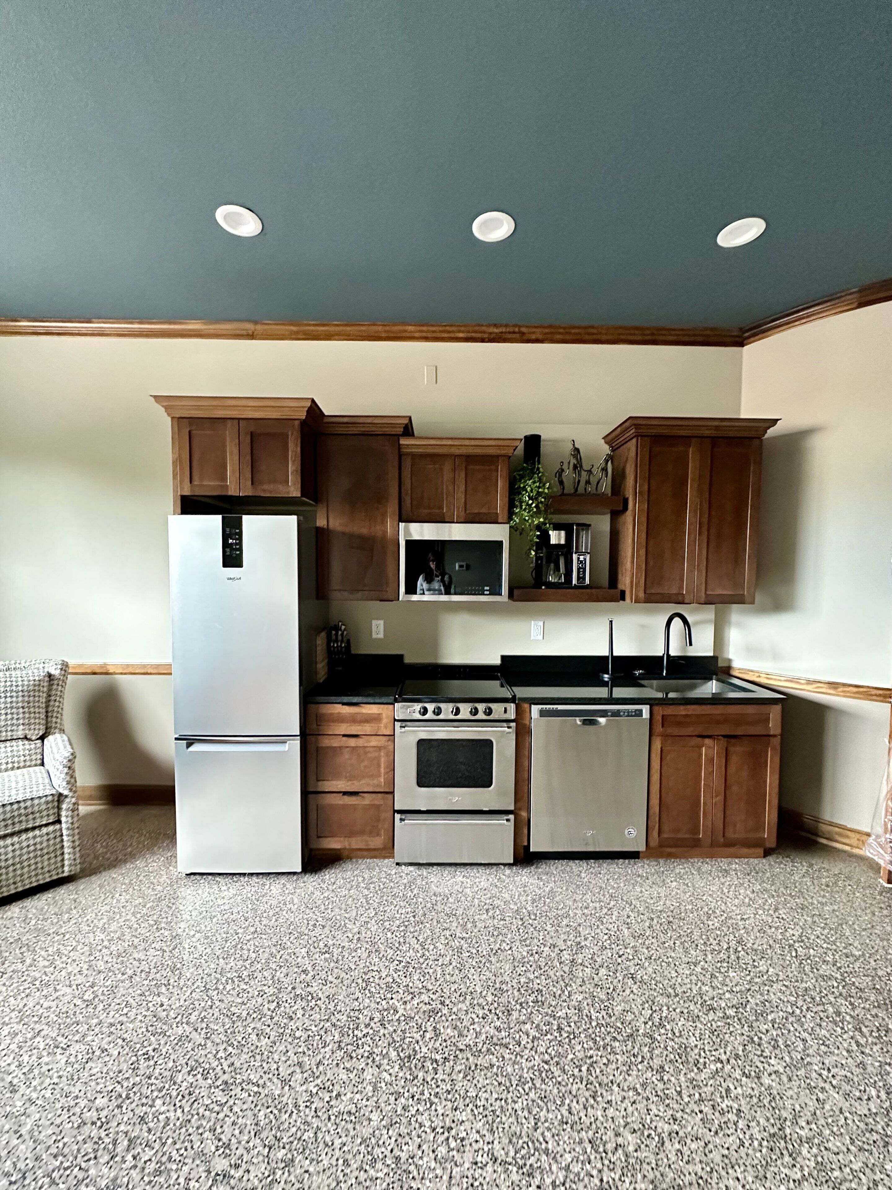 A kitchen with wooden cabinets, stainless steel appliances, and a houndstooth-patterned chair.
