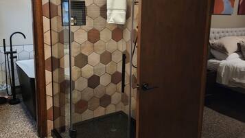 Une salle de bain dotée d’une douche à parois de verre, d’un lavabo blanc et d’un mur décoré de carreaux formant un motif hexagonal.