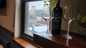 A window with a view of a bridge and buildings, a bottle of wine, and two wine glasses on a wooden ledge. - The Lodge Luxury Suites (Hancock)