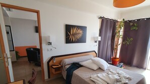 Une chambre d’hôtel avec un lit, un bureau, une chaise, une plante en pot et un tableau au mur.