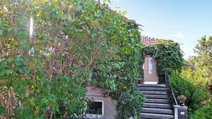 Un escalier en pierre mène à une porte portant le numéro 10, qui est entourée d’une végétation luxuriante et s’ouvre sur un ciel dégagé.