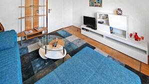 Un salon moderne comprenant un canapé, une table basse en verre, un téléviseur et une étagère blanche où sont disposés des objets décoratifs.