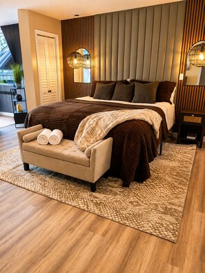 A bedroom with a large bed, a sofa, a bedside table, and a potted plant.