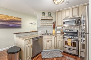 Una cocina con armarios color beige, electrodomésticos de acero inoxidable, encimera de granito y un cuadro decorativo en la pared.