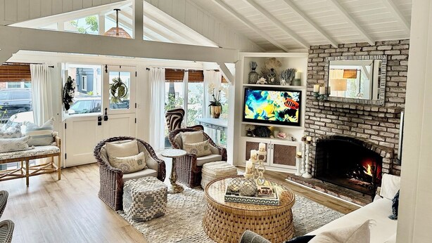 A cozy living room with wicker furniture, a fireplace, and a television. - Balboa Island Beach Cottage (Newport Beach)
