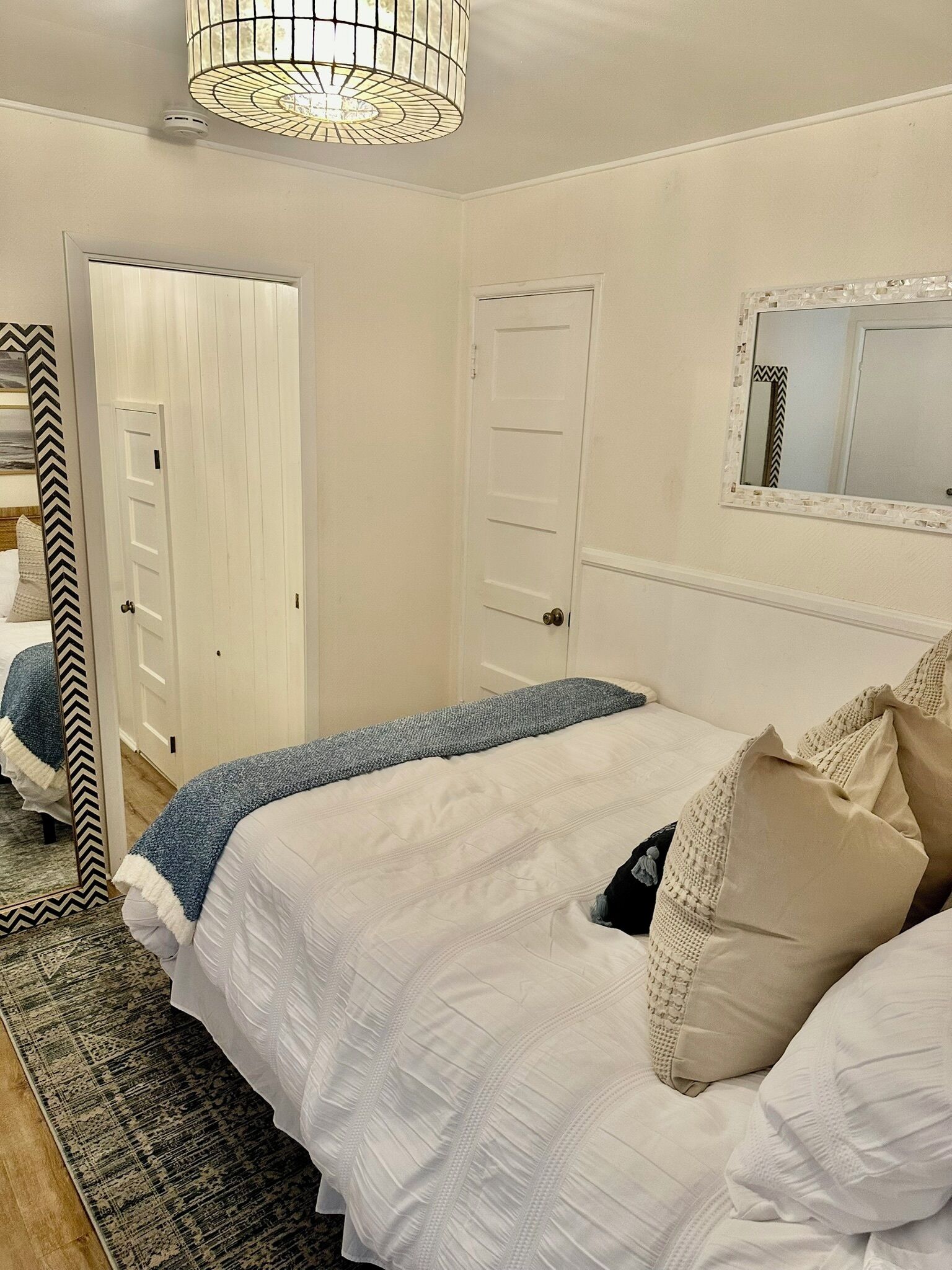 A bedroom with two beds, a large mirror, and a hanging light fixture.