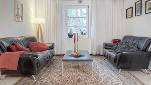 Ett vardagsrum med två lädersoffor, ett soffbord och en mönstrad matta. Det finns ett fönster med gardiner, en golvlampa och inramade tavlor på väggen.