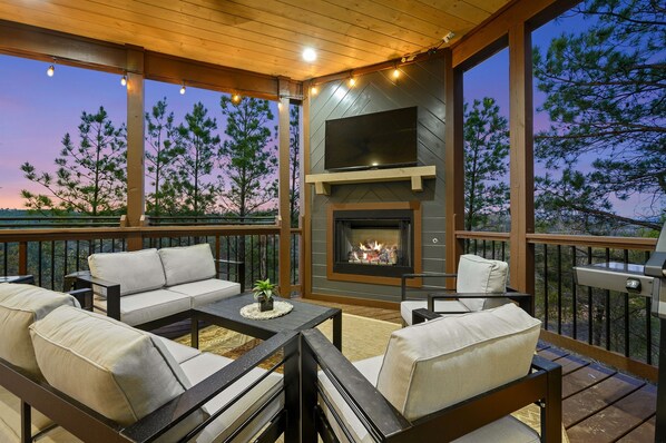 A deck with a fireplace, outdoor seating, and a view of trees. - Panoramic Mountain Views | Spacious Lodge (Broken Bow)