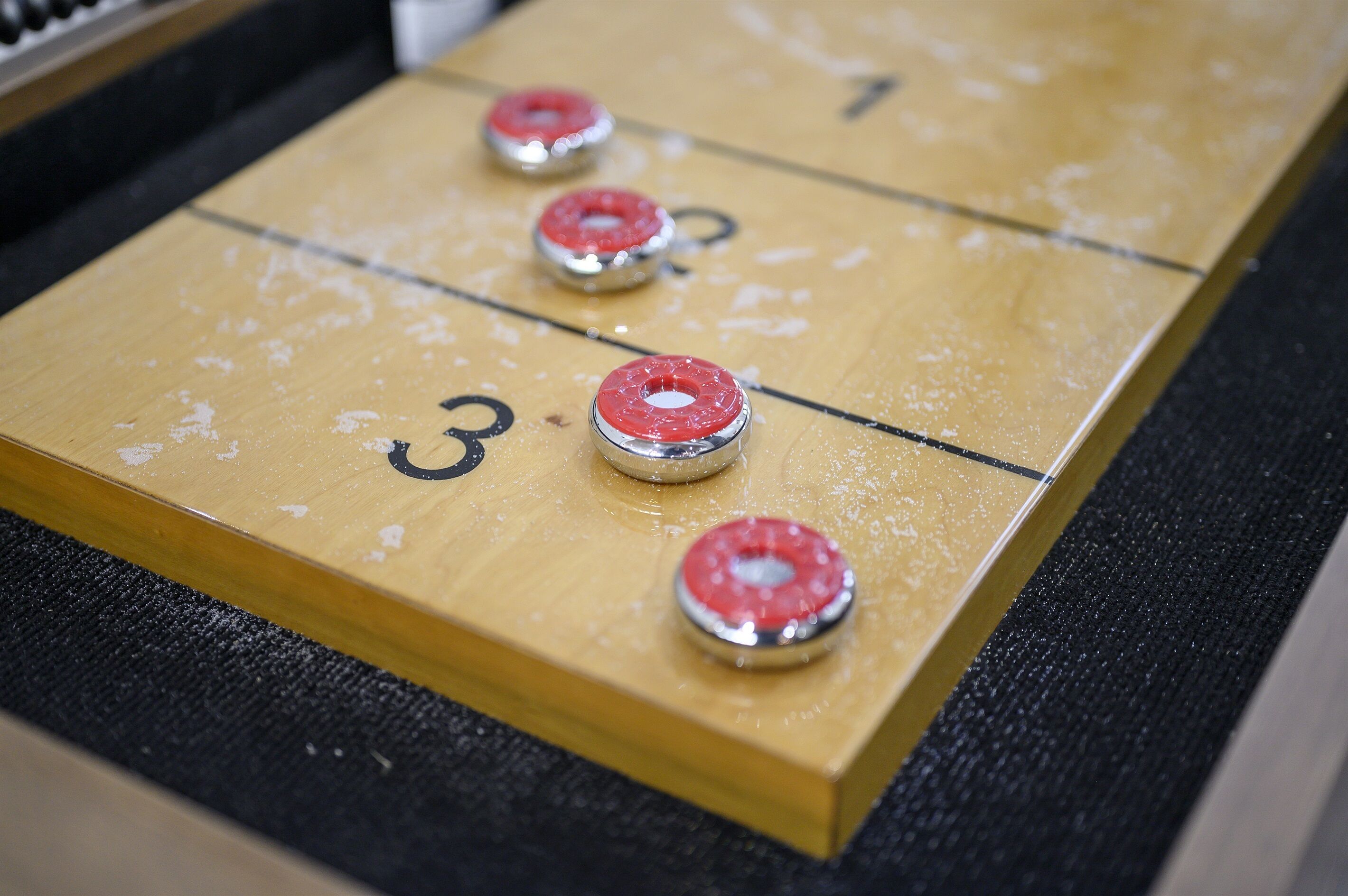 Una mesa de shuffleboard con zonas de puntuación numeradas y discos.