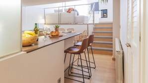 Una cocina moderna con una isla central, un área de comedor con sillas y una escalera que sube a un nivel superior.