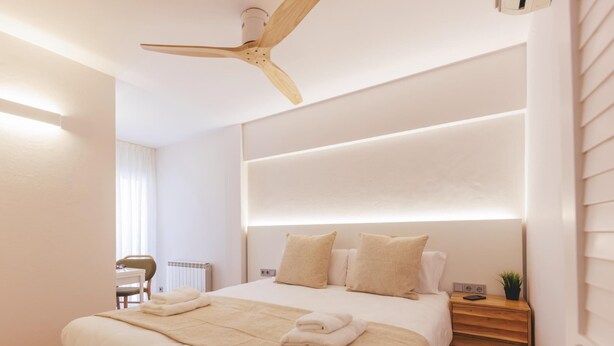 Un dormitorio moderno con una cama grande, mesitas de noche, ventilador de techo y radiador.