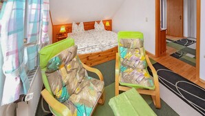 A bedroom with a bed, two chairs, a nightstand, a lamp, and a door.