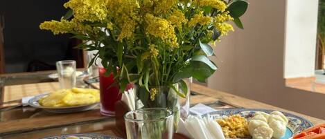 Una mesa de comedor con platos de comida, un florero con flores amarillas y una cesta de pan.