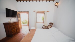 Un dormitorio con cama, cómoda de madera, televisor y ventana con cortinas.