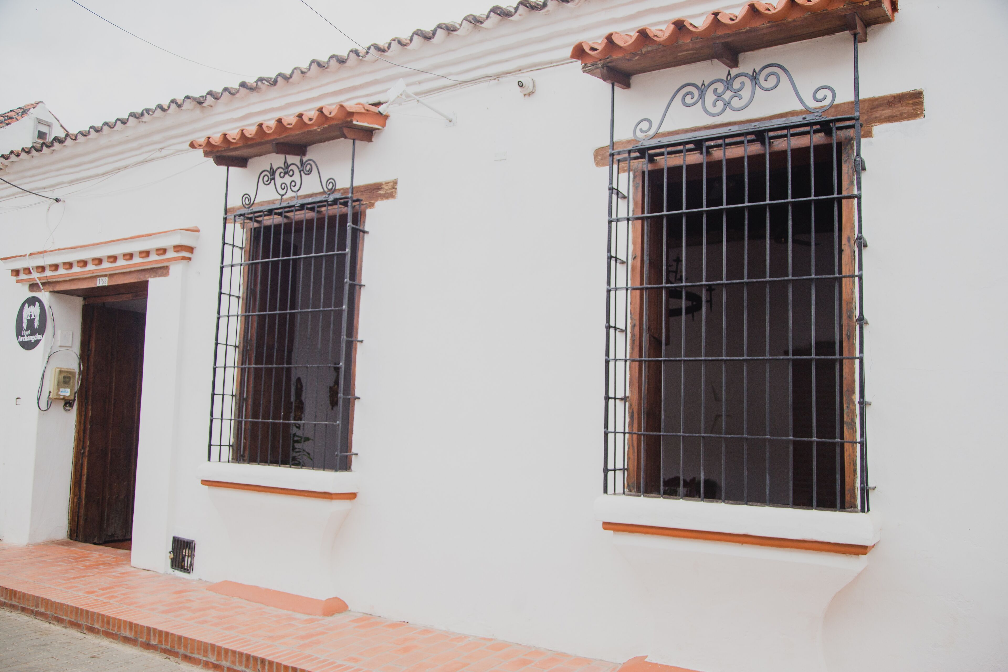 Un edificio blanco con dos ventanas de celosía y una puerta, que cuenta con un tejado de tejas y un porche pequeño.