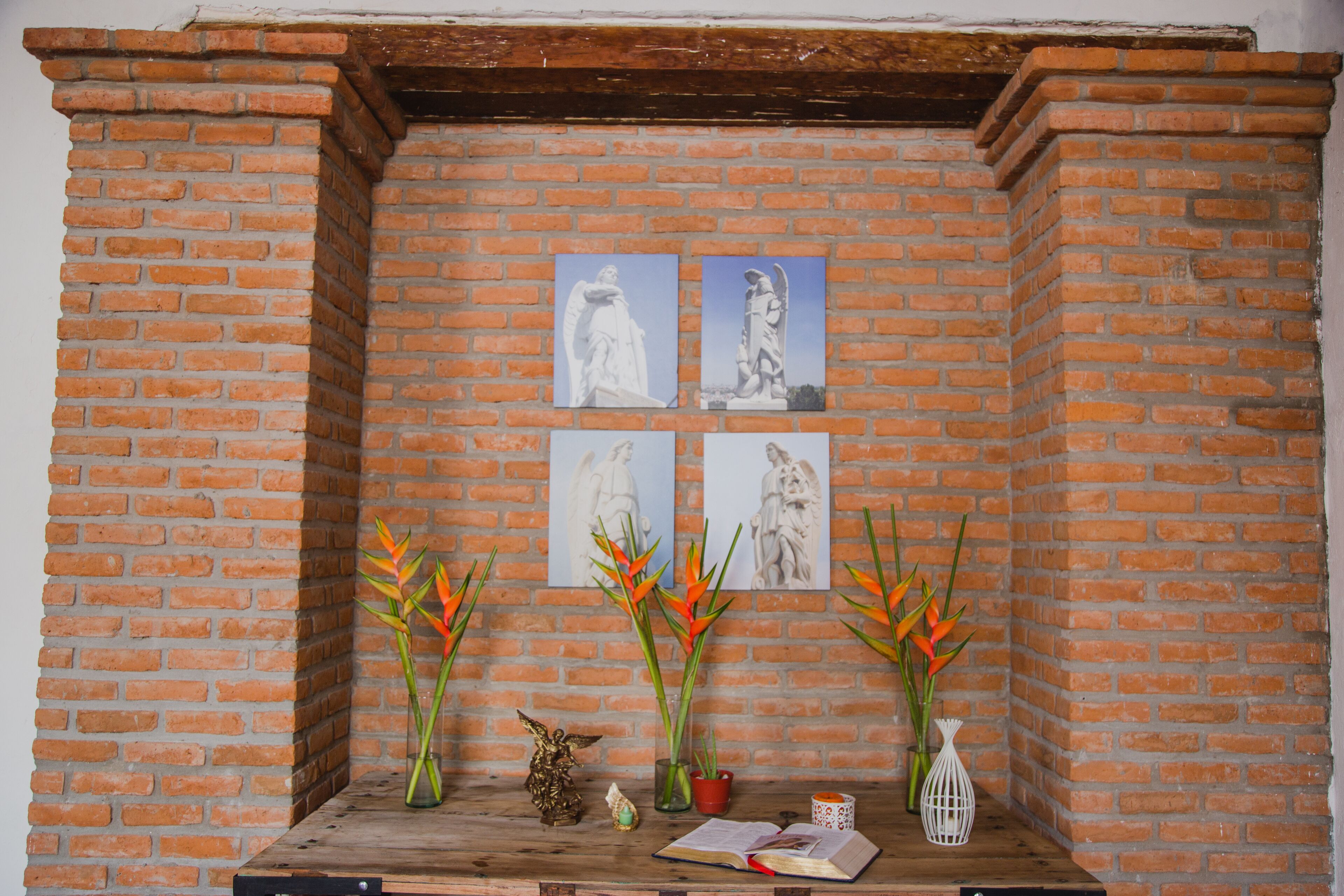 A brick wall with four framed artworks and two vases with orange flowers.