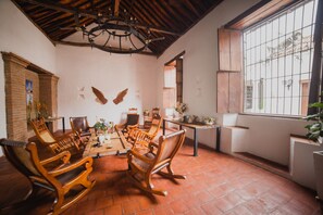 A dining area with wooden chairs and a table, a brick wall with a mural, and a window with bars. - Hotel Archangelus (Mompos)