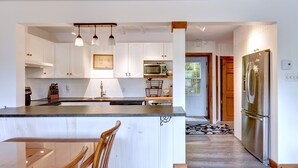 Una cocina moderna con armarios blancos, una isla central, un refrigerador de acero inoxidable e iluminación colgante.