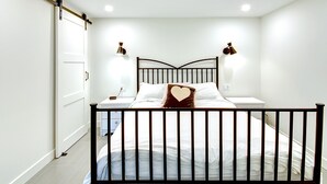 Un dormitorio con una cama, dos lámparas de noche, una mesita de noche y un almohadón con forma de corazón.