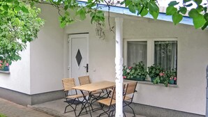 Un área de estar al aire libre con una mesa, sillas y plantas en macetas. También se observa una puerta blanca.