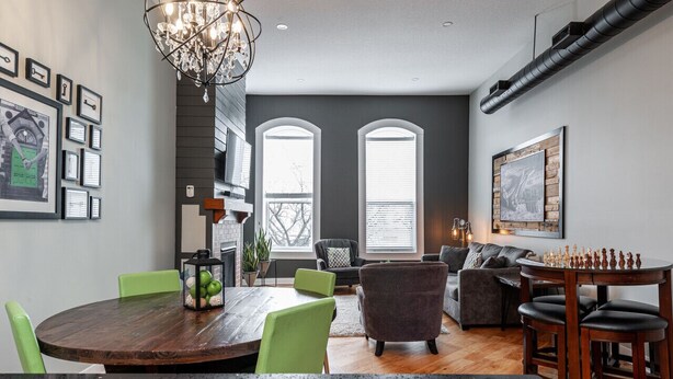 A modern dining area with a wooden table, green chairs, and a chandelier. - River Merchant Inn Mitchell’s Mercantile Suite (Stratford)