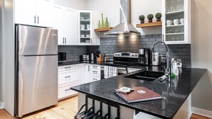 A modern kitchen with stainless steel appliances, white cabinets, a black countertop, and a central island. - River Merchant Inn Mitchell’s Mercantile Suite (Stratford)