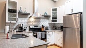 A modern kitchen with white cabinets, a stainless steel refrigerator, a built-in oven, and a gas stove. - River Merchant Inn Heintzman Music Suite (Stratford)