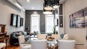 A modern living room with a glass coffee table, two sofas, a piano, and a large painting. - River Merchant Inn Heintzman Music Suite (Stratford)