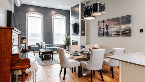 A modern living room with a piano, a dining area with a glass table, and a kitchen with a TV. - River Merchant Inn Heintzman Music Suite (Stratford)