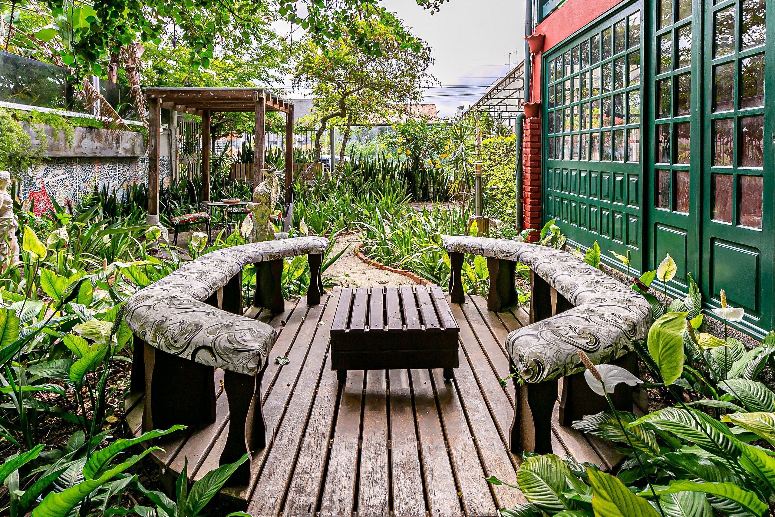 A wooden deck with a bench in the center, surrounded by lush greenery and a pergola.
