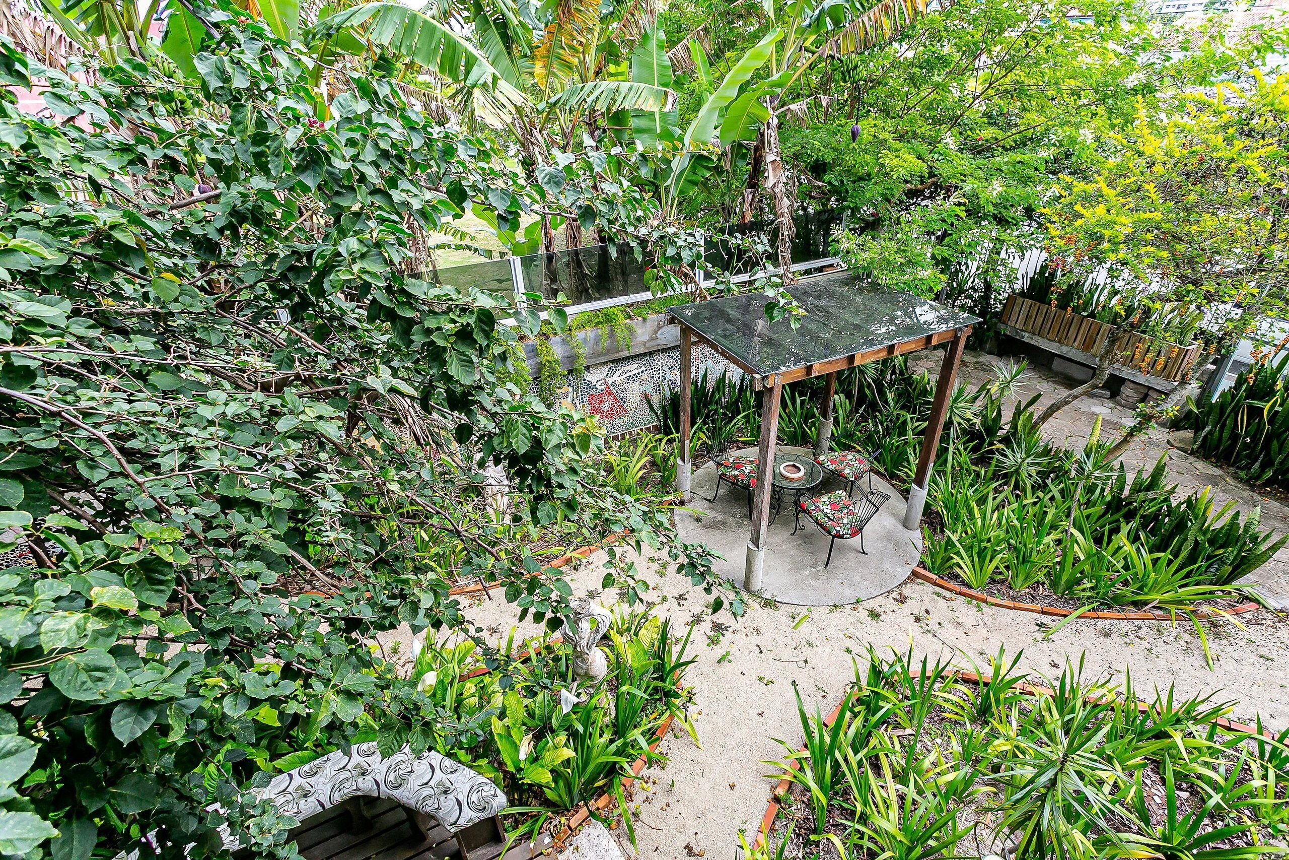 A garden area with a wooden table and chairs, surrounded by various plants and a small pond.