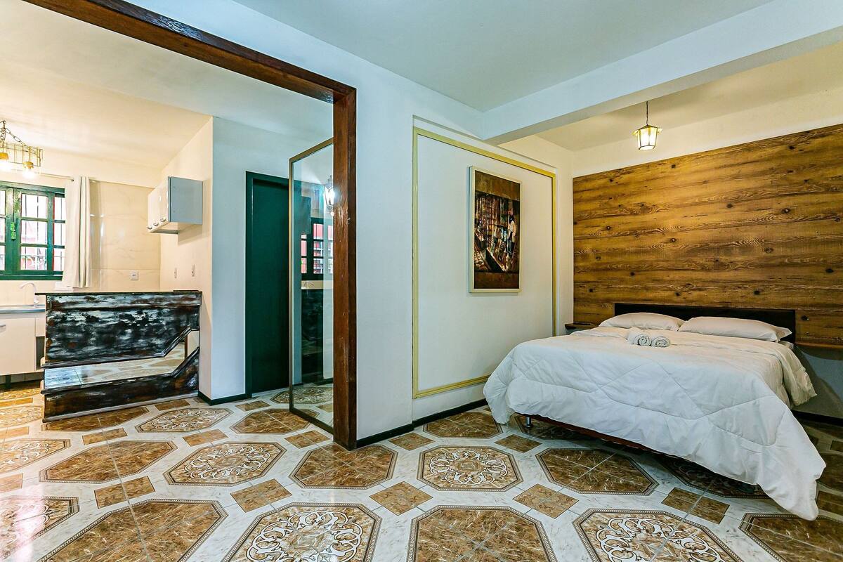Une chambre à coucher avec un lit, une tête de lit en bois, un grand miroir et un sol à motifs.