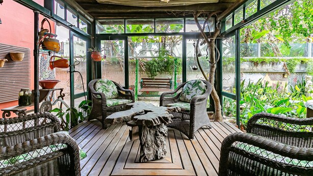Un patio cubierto con mobiliario de mimbre, una mesa de madera y plantas en macetas.
