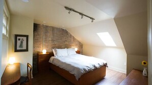 Ein Schlafzimmer mit schrägem Dach, einem Bett, einem Nachttisch, einem Sessel und einem Bild an der Wand.