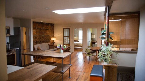 Amplia sala de estar con una mesa de comedor de madera, un sofá y una cocina con refrigerador.