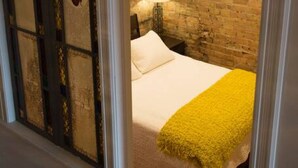 Un dormitorio con cama, mesita de noche, lámpara y pared de ladrillo.