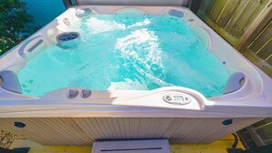 Un bain à remous doté d’un panneau de commande, de haut-parleurs intégrés et d’une terrasse en bois qui l’entoure.