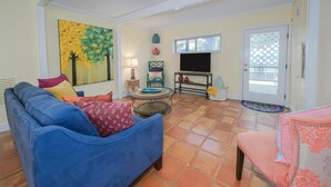 Un salon avec un canapé bleu, un fauteuil rose, un téléviseur et un tableau accroché au mur.