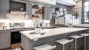 A modern kitchen with a large island, bar stools, and a view of the outdoors through a large window. - Bradshaw Lofts:  La Galleria (Stratford)