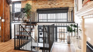A spacious loft with exposed brick walls, a mezzanine level, and a modern staircase. - Bradshaw Lofts:  La Galleria (Stratford)