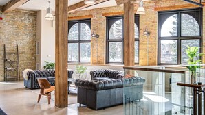 Un vaste espace de vie de style « loft », avec des poutres apparentes, de grandes fenêtres et un mélange de meubles en cuir et en tissu.