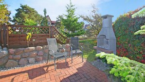 An outdoor patio with a stone wall, two metal chairs, a wooden fence, and a stone chimney. - Ferienwohnung Karlshagen (Karlshagen (Ostseebad))