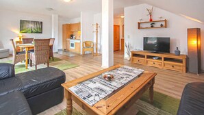 A spacious living room with a wooden coffee table, a television, and a dining area with wicker chairs. - Ferienwohnung Karlshagen (Karlshagen (Ostseebad))