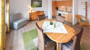 A cozy living room with a sofa, a dining table with chairs, a kitchen area, and a painting on the wall. - Ferienwohnung Karlshagen (Karlshagen (Ostseebad))