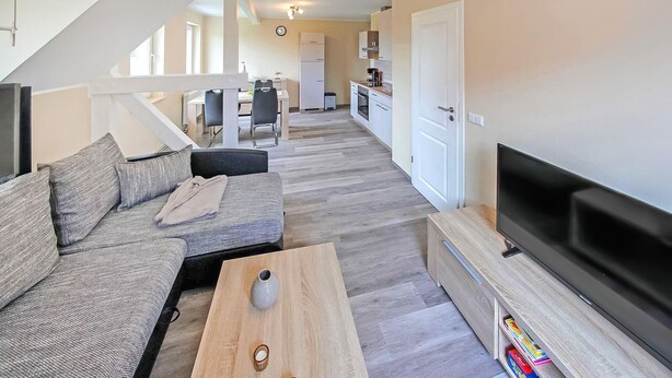 A modern living room with a sofa, coffee table, TV, and a kitchen in the background. - Cozy apartment in Mirow with WiFi (Mirow)